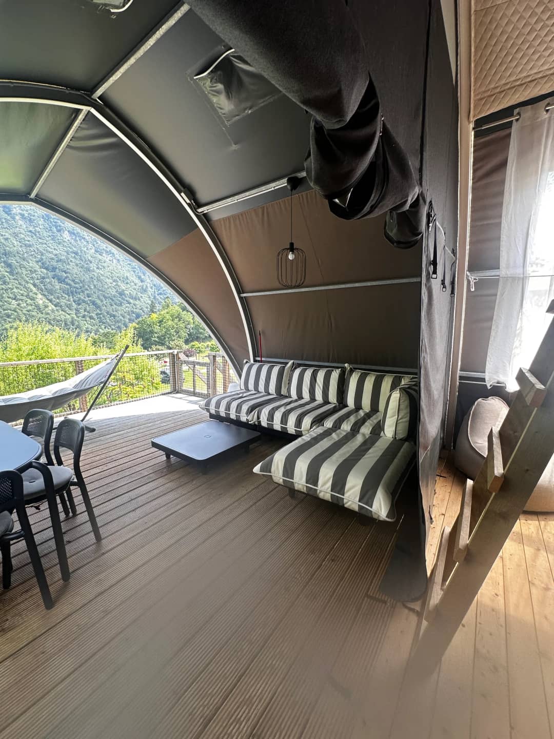 The covered veranda at the Big Oak Lodge XL, featuring a striped lounge sofa, coffee table and dining table, with views of the mountains
