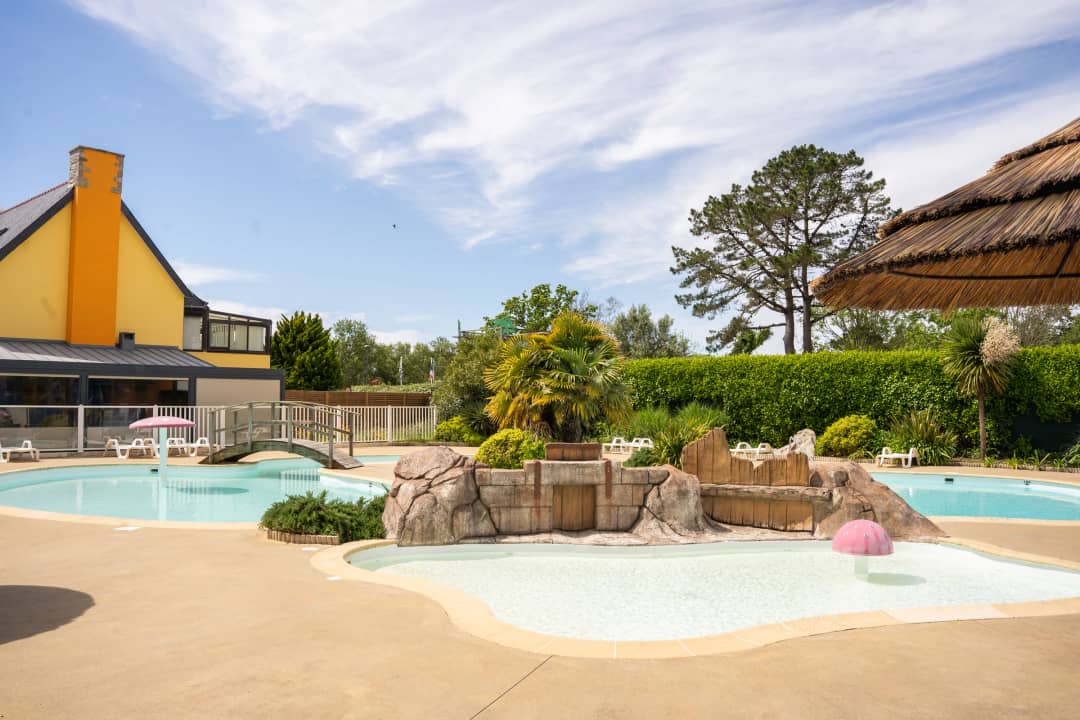Swimming pool with a water feature and palm trees near the yellow buildings