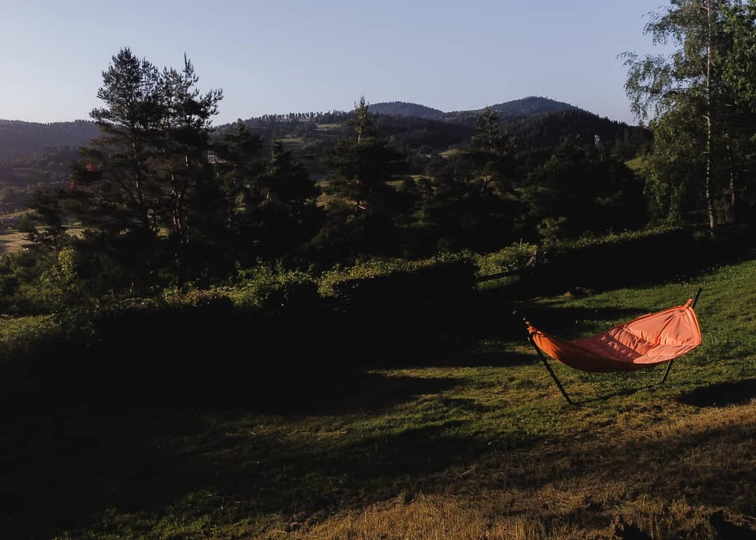 A grassy field with a hammock and mountains in the last light of day