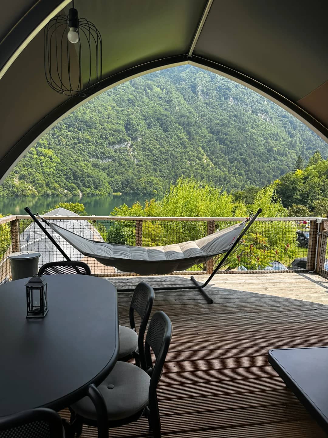 A hammock and a dining table with a lantern on the veranda of the Big Oak Lodge XL, overlooking the lake and the mountains
